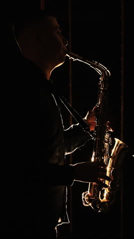 Vertical Format Video of Black silhouette of male saxophonist musician playing golden alt saxophone on musical instrument. Cool saxophone player performing a solo on stage. Musician playing in band.