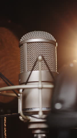 Vertical Format Video of Professional microphone and headphones at sound record studio. Microphone on stage against a black background with lighting. Recording concept. Slow motion in 100 fps