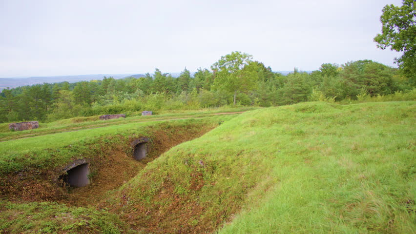 Wide shot of a grassy field with two concrete bunkers in the middle. A couple of bunker entrances in a grassy knoll on a historical battlefield site