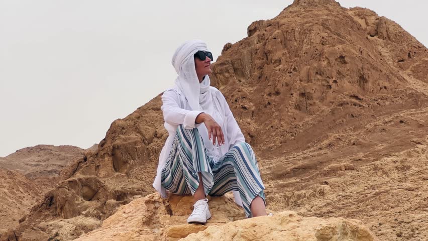 Stylish female with glasess sitting on a rock in the Sahara desert near Chebika oasis