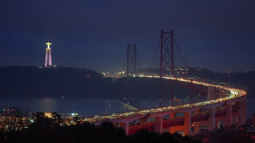 Bridge from Miradouro do Bairro do Alvito tourist viewpoint with Tagus river, traffic on 25th of April Bridge in the dark against the backdrop of a statue of Christ. Lisbon, Portugal