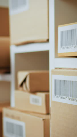 A warehouse worker uses an electronic scanner to read a barcode on a cardboard box. This activity helps in tracking inventory and streamlining the shipping process in a busy warehouse setting