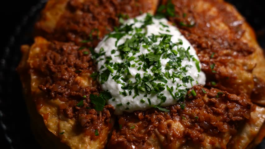 Traditional Turkish food Kayseri Yaglamasi with minced meat, oily, tomato paste and topped with yogurt. Layered yaglama dish garnished with parsley on black background. Anatolian cuisine and flavors 