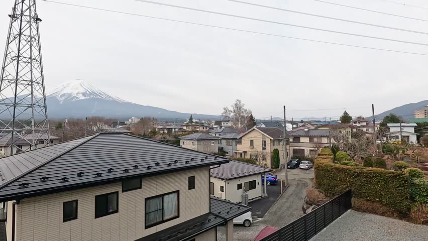 A serene view of Mount Fuji over a residential area in Kawaguchiko, Japan, captured on a cloudy day with static camera framing