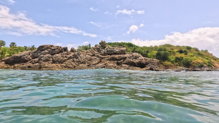 Calm ocean waters and rocky shoreline under a bright sky at Yanui Beach, Phuket, Thailand. Captured with steady camera movement
