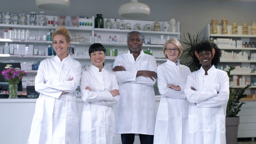 Diverse team of pharmacists standing together in modern pharmacy, smiling confidently with arms crossed, showcasing teamwork and professionalism