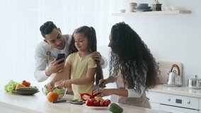 A Middle Eastern family gathers in a modern kitchen, preparing a meal with fresh vegetables. The father captures a moment on his phone as the mother helps their daughter chop ingredients. - Powered by Shutterstock - Get 15% off with code: PIKWIZARD15