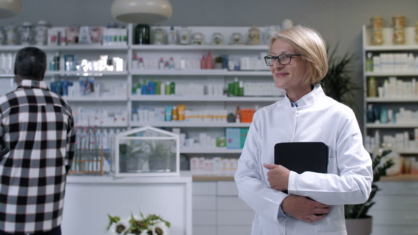 Pharmacist showing medicine to customer holding mobile phone, providing healthcare advice in pharmacy setting