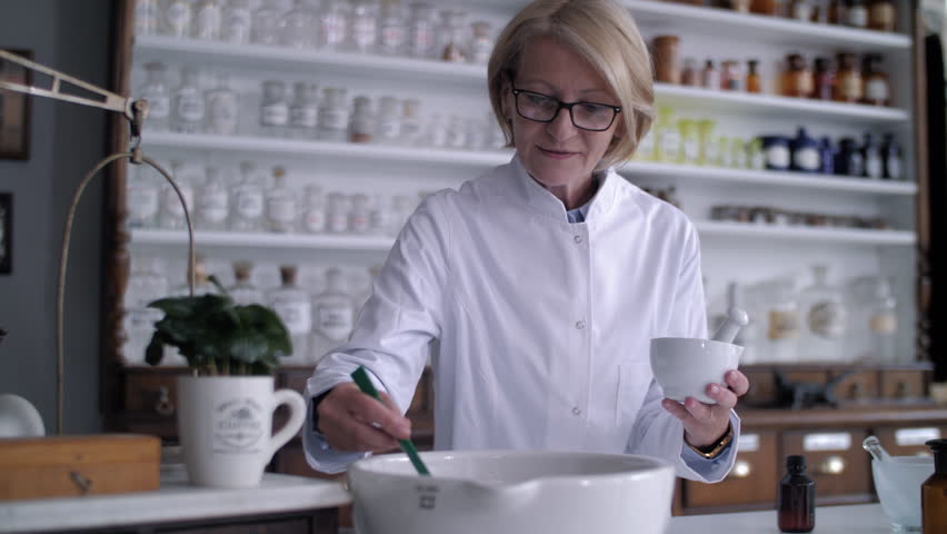 Senior female pharmacist mixing ingredients in a mortar and pestle inside a traditional pharmacy