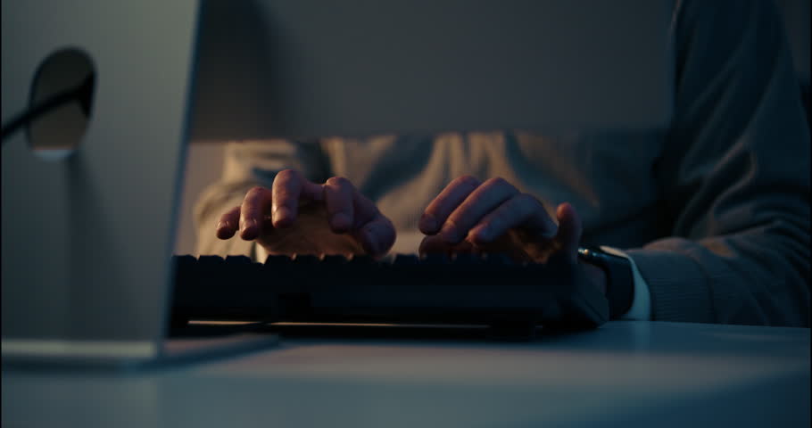 Close-up of a man’s hands typing on a keyboard in low light. Dark tech environment, hacker or night programmer theme with intense focus and secrecy.