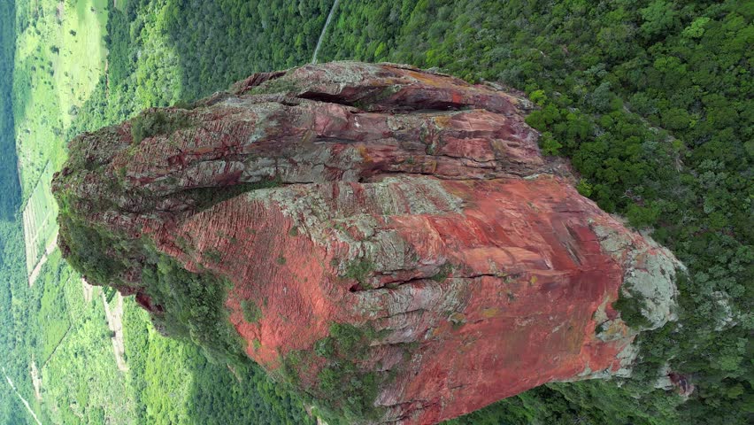 Vertical aerial tilts to reveal green valley below red rock stone tower