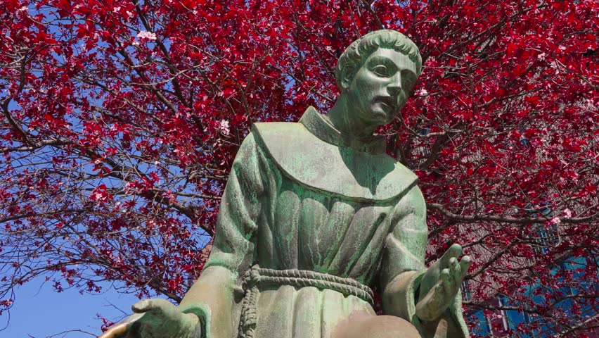 Low angle shot of a saint statue with water from a fountain reflecting on it and bright red leaves trees in the background in Milan Milano Italy