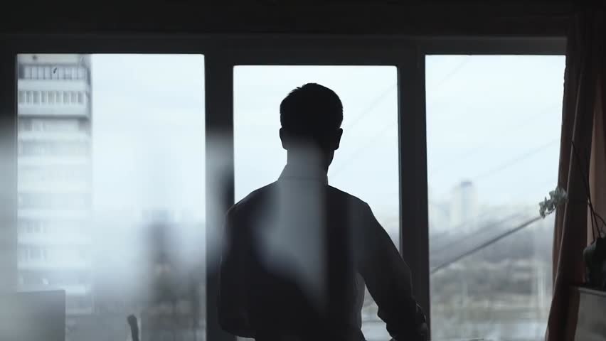 Slow-motion shot of a man in a stylish suit standing near a window, adjusting his attire. Preparing for a wedding or festive reception, he exudes confidence, elegance, and anticipation.