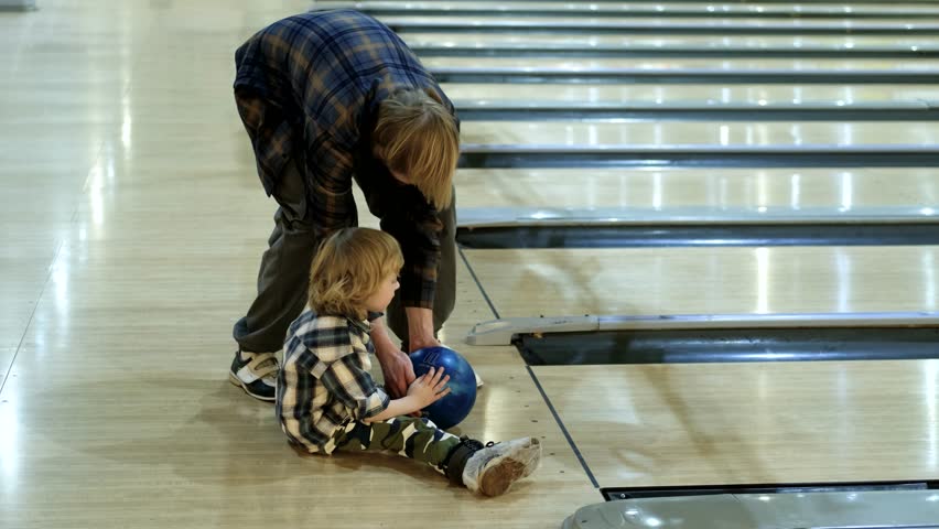 father and son throwing a ball on a bowling alley