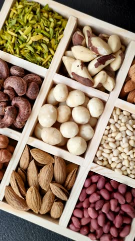 Mix of macadamia, pine, cashew, hazelnut, peanut, pistachio nuts in a wooden box with several sections
