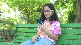 Happy indian girl kid wearing spectacles using smart phone at summer park, addiction and wireless technology. 5G network. Watching videos, Social media, Entertainment. - Powered by Shutterstock - Get 15% off with code: PIKWIZARD15