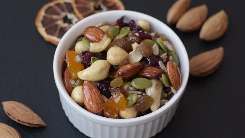 Honeyed cashew nuts, walnuts, hazelnuts, pine nuts and dried fruits in ceramic bowl on dark concrete background