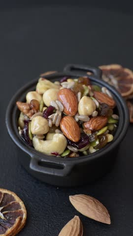 Honeyed cashew nuts, walnuts, hazelnuts, pine nuts and dried fruits in ceramic bowl on dark concrete background