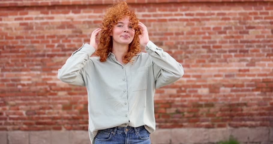Young redhead woman posing and smiling against a brick wall background