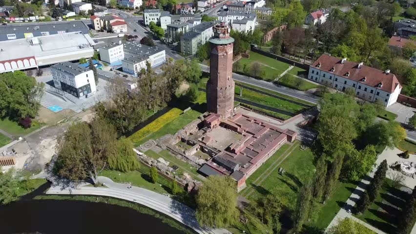 A drone explores the ruins of a historic castle in the heart of a Polish town. Only one tower remains, surrounded by urban scenery blending past and present.