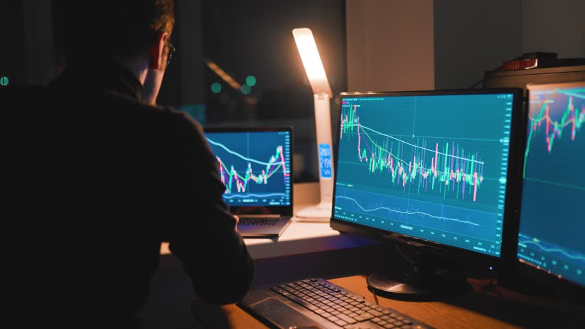 A trader analyzes data and market trends on multiple screens in a modern workspace at night. Focus and analysis are key as they work with charts and graphs to execute trades. - Powered by Shutterstock - Get 15% off with code: PIKWIZARD15