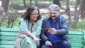 Happy retired senior Indian couple using smart phone at park, old man and woman watching video social media on mobile phone. Wireless Technology, 5G Network, Entertainment, Retirement life. - Powered by Shutterstock - Get 15% off with code: PIKWIZARD15