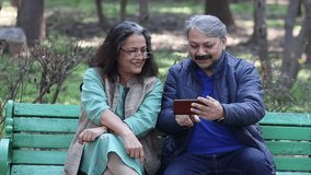 Happy retired senior Indian couple using smart phone at park, old man and woman watching video social media on mobile phone. Wireless Technology, 5G Network, Entertainment, Retirement life. - Powered by Shutterstock - Get 15% off with code: PIKWIZARD15