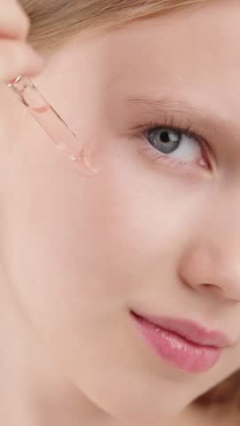 A young Gen Alpha girl with flawless, radiant skin applies a skincare serum to her face using a dropper. Close-up shot highlights her smooth complexion. Concept of beauty, skincare for kids and teens 