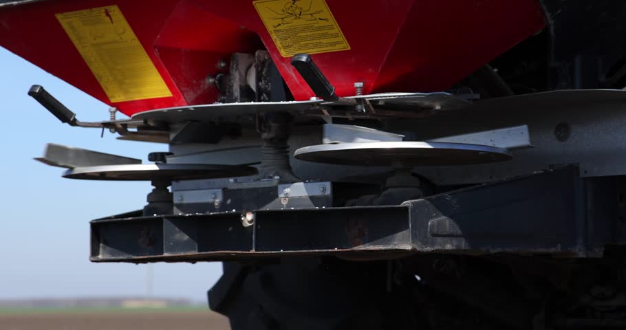 Farmer with agricultural machinery fertilizing agricultural field in spring time, slow motion. Spreading mineral fertilizer, low angle shot