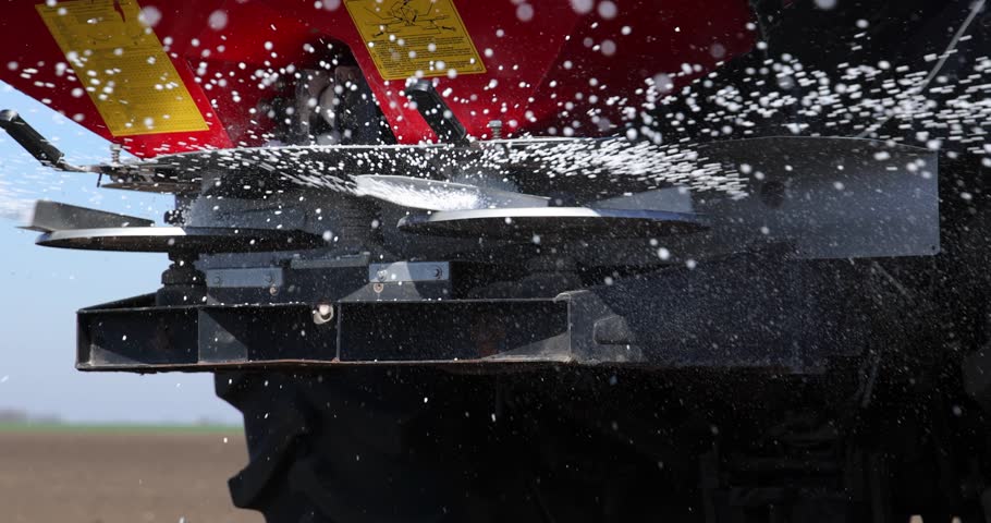 Farmer with agricultural machinery fertilizing agricultural field in spring time, slow motion. Spreading mineral fertilizer, low angle shot