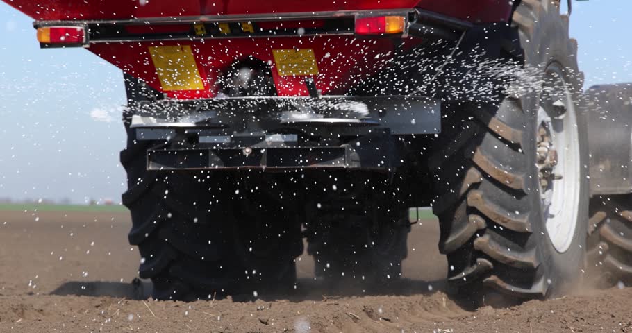 Farmer with agricultural machinery fertilizing agricultural field in spring time. Spreading mineral fertilizer, low angle shot