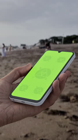 GREEN SCREEN CHROMA KEY Person holding a smartphone at a scenic beach during sunset with silhouettes of people and waves in the background