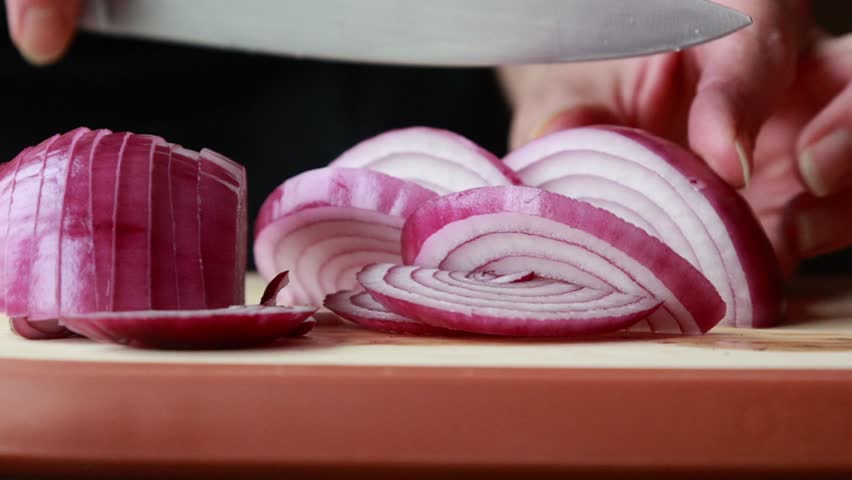  woman slicing red onion on wooden cutting board close-up