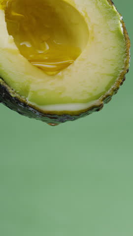 Oil is dripping down from cut in half avocado fruit. Conceptual slow motion vertical template.