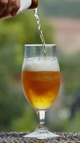 Pouring beer in the glass. Blurred green nature in the background.