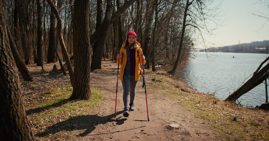 Backpacker hiker girl with hiking poles walking between trees in a mountain forest. Hispanic teenager in the woods.