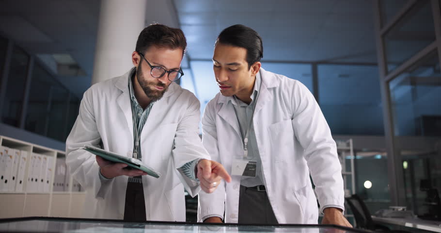 Scientist, talking and teamwork with tablet in laboratory for pharmaceutical review, medical research or innovation. Night, people and interactive display for studying science, meeting and results
