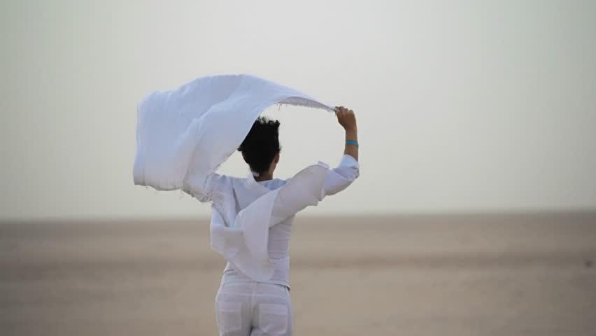 Running woman waving white scarf in Sahara desert landscape during sunrise