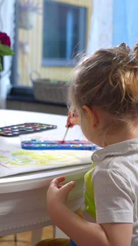 A cheerful young child enjoys painting with bright watercolors at home. Focused and happy, he creating a colorful artwork. The cozy interior, soft lighting, and creative atmosphere highlight a moment