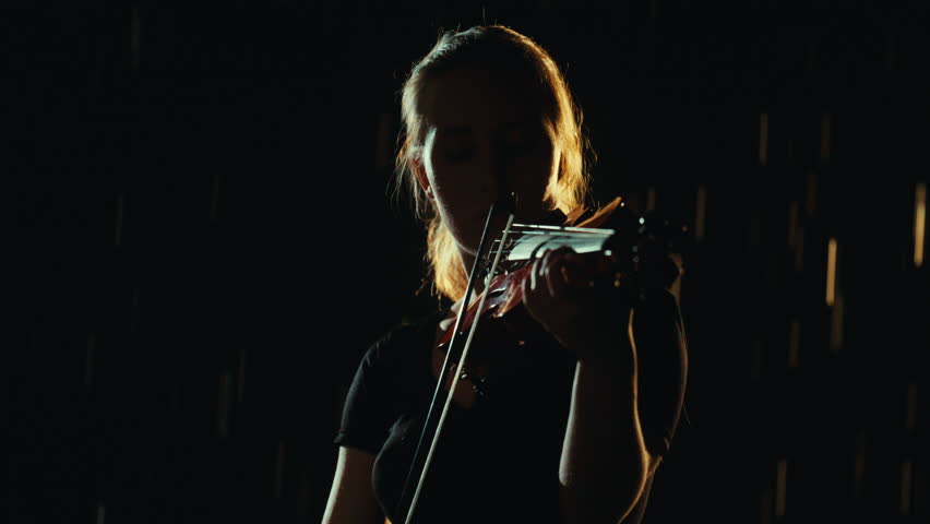 Female student rehearsing melody, playing violin in darkness, slow motion shot. Beautiful classical music, mysterious night rain, lady expressing her emotions and feelings, talent and inspiration