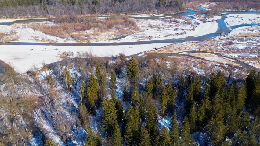 Aerial view of a winter river landscape with meandering streams, sandy banks, and snow-covered trees in a peaceful natural environment