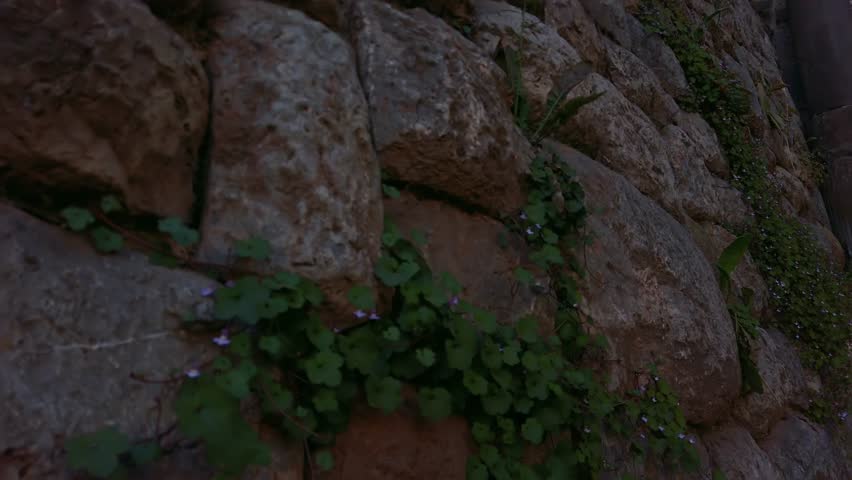 Colonial stone arch with ornate crest, columns, and spires under blue sky in Cusco. Pan right shot reveals Arco de Santa Clara, historic stone arch in Cusco, Peru