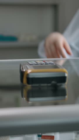 A man pays for a prepared order at a pharmacy by credit card on terminal. Close-up of a bank transaction with a plastic card in a pharmacy. No faces. Vertical shot.