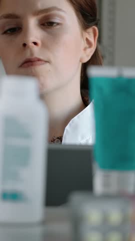 The girl pharmacist conducts an audit of medical products in the pharmacy. Caucasian woman with an electronic tablet checks the presence of drugs creams and tablets on the shelf in the pharmacy