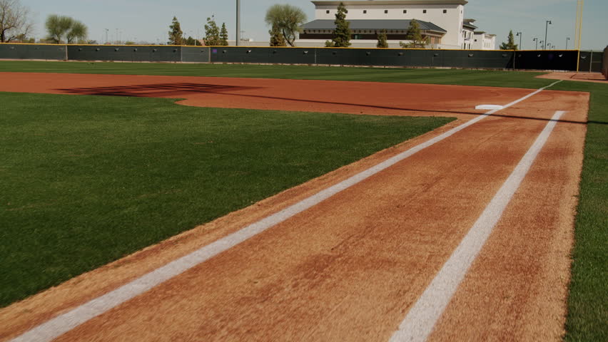 A drone footage of an empty, clean Baseball Field under clear sky, with modern building in distance in Texas