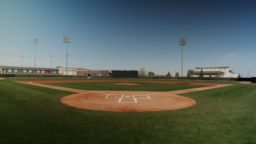 A drone footage of an empty, clean Baseball Field under clear sky, with buildings in distance in Texas