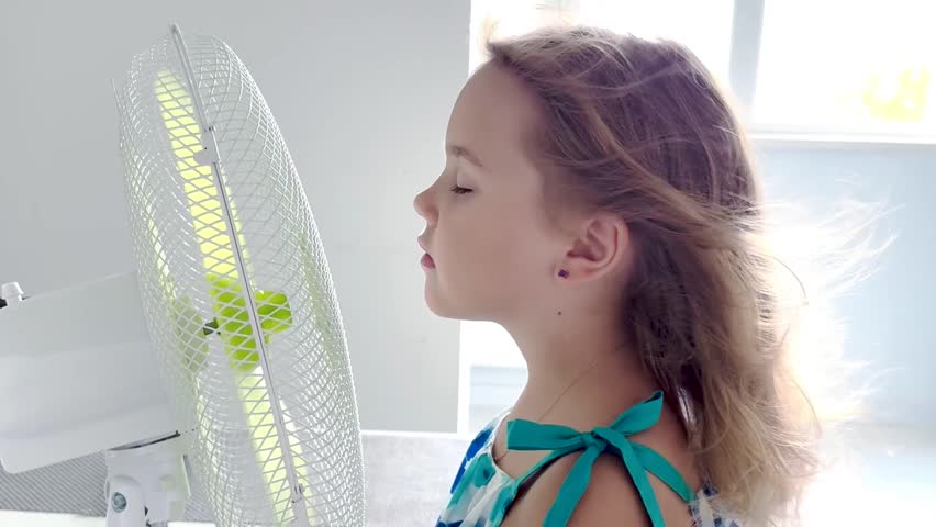Caucasian child girl enjoing cool blowing air in front of fan, summer heat concept,hot weather and refreshment,cooling person.
