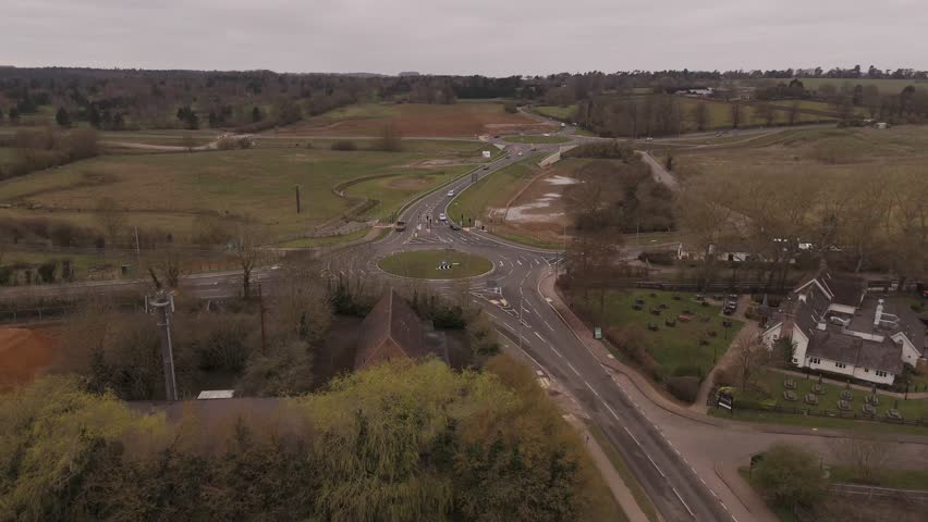 4K static drone footage showing a UK roundabout with active traffic, set in a rural landscape near the start of Brampton Valley Way. The camera is positioned at an elevated angle, capturing the road l