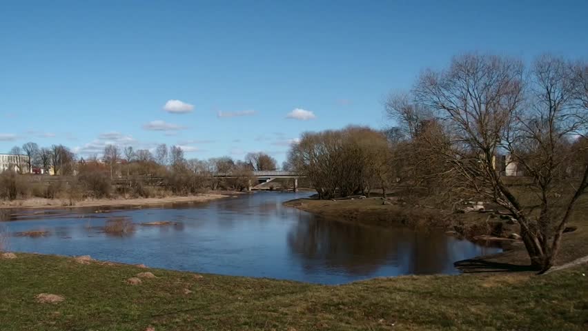 River Flow on Sunny Day: Calm Water with Bridge and Bare Trees, Peaceful Nature Scene, Showing Spring Landscape and Clear Sky