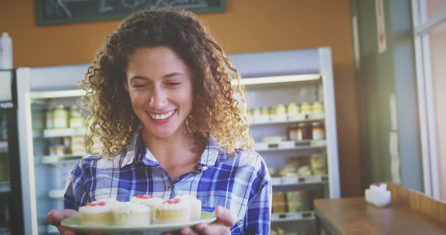 Holding cupcakes in bakery, smiling woman with shelves in background. pastries, desserts, baking, happiness, kitchen, culinary